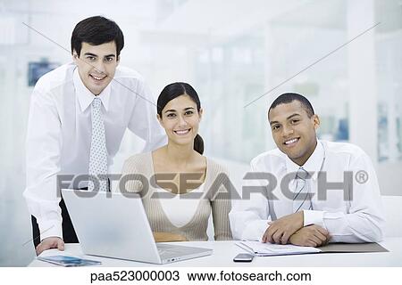 Professionals gathered around laptop computer, smiling at camera View Large Photo Image Stock Image - Professionals gathered around laptop computer, smiling at camera. Fotosearch