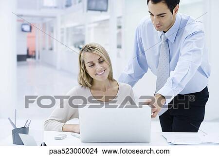 Professionals looking at laptop computer together, man looking over woman's shoulder View Large Photo Image Picture - Professionals looking at laptop computer together, man looking over woman's shoulder. Fotosearch