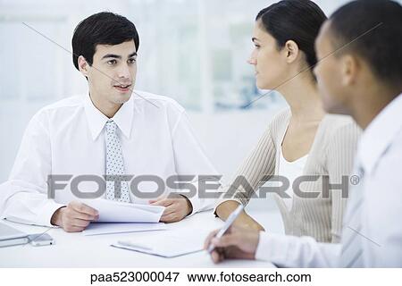 Stock Photo - Professionals sitting at table, discussing documents. Fotosearch