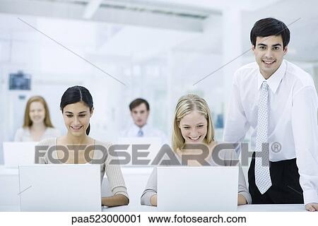 Supervisor standing beside employees working on laptops, smiling at camera View Large Photo Image Stock Image - Supervisor standing beside employees working on laptops, smiling at camera. Fotosearch