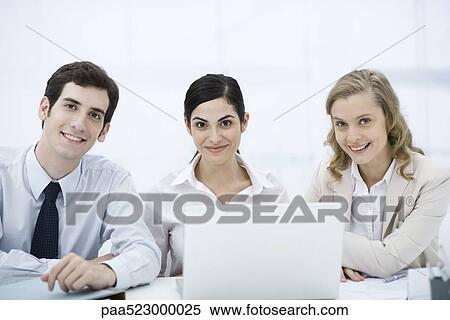 Team of professionals sitting with laptop computer, smiling at camera View Large Photo Image Stock Photography - Team of professionals sitting with laptop computer, smiling at camera. Fotosearch
