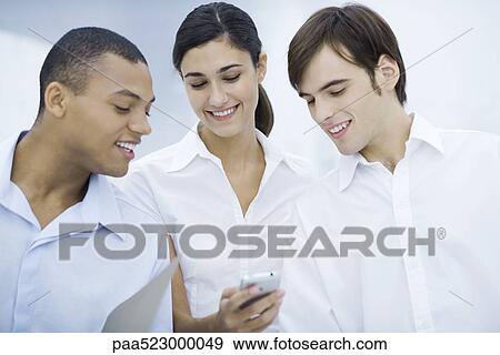 Three young professionals looking at cell phone together, smiling View Large Photo Image Stock Photo - Three young professionals looking at cell phone together, smiling. Fotosearch