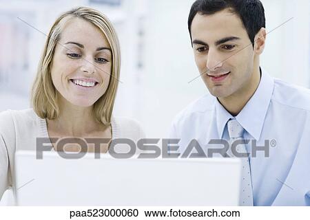 Two professionals looking at laptop computer together, smiling View Large Photo Image Stock Image - Two professionals looking at laptop computer together, smiling. Fotosearch