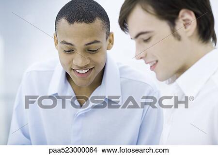 Two young men looking down, smiling View Large Photo Image Picture - Two young men looking down, smiling. Fotosearch