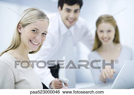 Young female professional smiling at camera, colleagues in background View Large Photo Image Stock Photograph - Young female professional smiling at camera, colleagues in background. Fotosearch