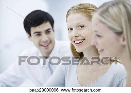 Young professional woman between two colleagues, smiling at camera View Large Photo Image Stock Photograph - Young professional woman between two colleagues, smiling at camera. Fotosearch
