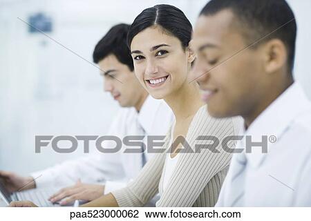 Young professional woman sitting between two male colleagues, smiling at camera View Large Photo Image Stock Image - Young professional woman sitting between two male colleagues, smiling at camera. Fotosearch