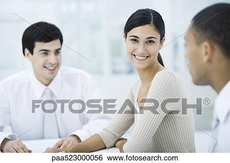 Stock Photograph - Young professional woman sitting with male colleagues, smiling at camera. Fotosearch