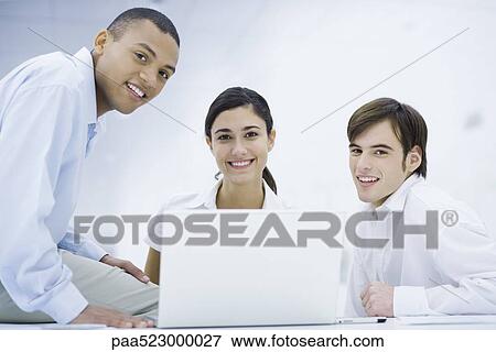 Young professionals gathered around laptop computer, smiling at camera View Large Photo Image Stock Photo - Young professionals gathered around laptop computer, smiling at camera. Fotosearch