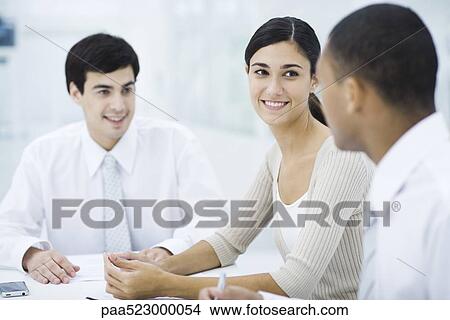 Picture - Young professionals sitting at table, focus on woman in center. Fotosearch