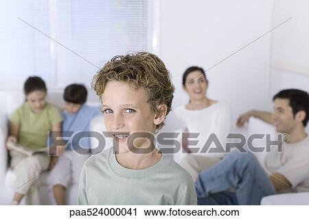Boy smiling at camera, family relaxing in background View Large Photo Image Stock Image - Boy smiling at camera, family relaxing in background. Fotosearch