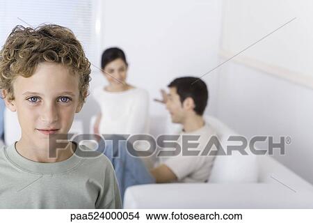 Picture - Boy smiling at camera, parents chatting in background. Fotosearch