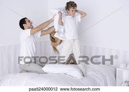 Stock Image - Family having pillow fight on bed. Fotosearch