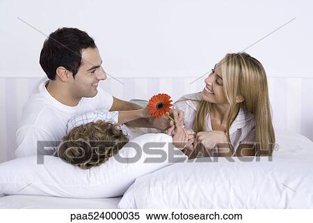 Stock Photography - Family lying in bed together, father and son giving mother a flower. Fotosearch