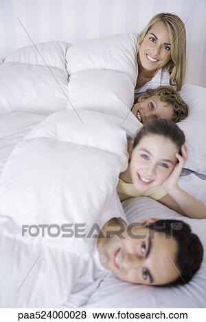 Stock Photo - Family lying in bed together, smiling at camera. Fotosearch