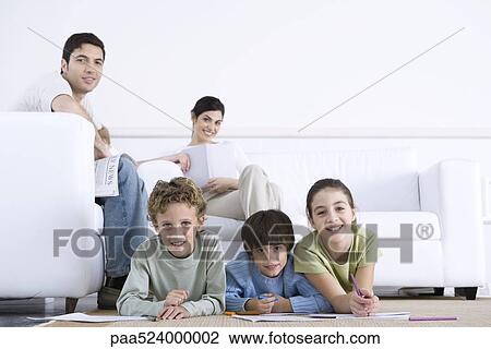 Stock Image - Family relaxing in living room, children coloring on the floor, parents sitting on sofa. Fotosearch