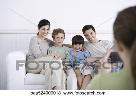 Stock Photo - Family sitting on sofa, posing for photo being taken by daughter. Fotosearch