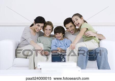 Stock Photography - Family sitting together on sofa, posing for digital camera set in foreground. Fotosearch