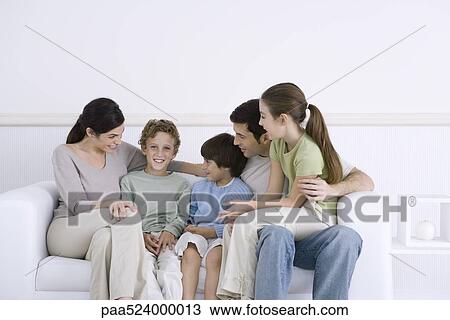 Family with three children sitting together on sofa, one boy smiling at camera View Large Photo Image Stock Image - Family with three children sitting together on sofa, one boy smiling at camera. Fotosearch