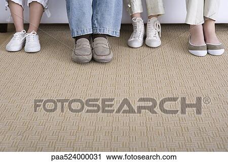 Stock Image - Four pairs of feet wearing different styles of shoes. Fotosearch