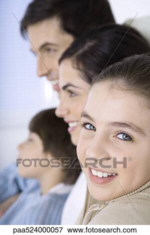 Stock Photo - Girl sitting with family, smiling over shoulder at camera, close-up. Fotosearch