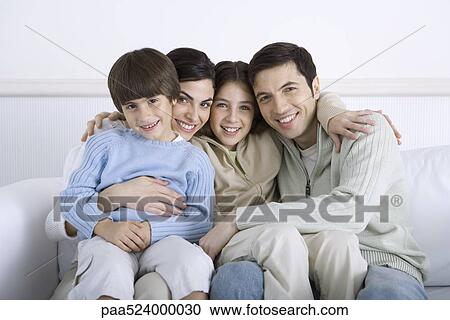 Stock Image - Parents and two children sitting together on sofa, portrait. Fotosearch