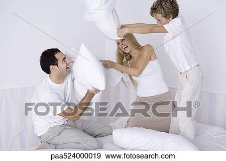 Parents and young son having pillow fight on bed View Large Photo Image Stock Photo - Parents and young son having pillow fight on bed. Fotosearch