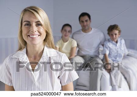 Portrait of smiling woman, family seated together on bed in background View Large Photo Image Stock Photo - Portrait of smiling woman, family seated together on bed in background. Fotosearch