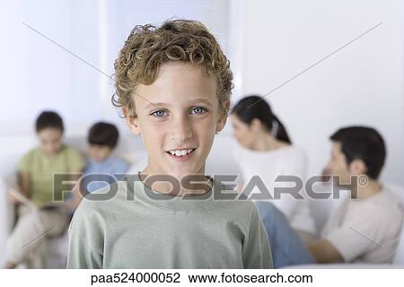 Stock Image - Portrait of smiling young boy, family seated in background. Fotosearch