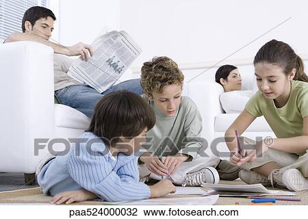 Stock Image - Three children sitting on the floor, coloring, parents reading in background. Fotosearch