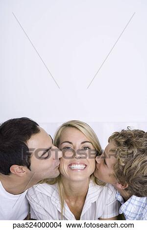 Picture - Woman being kissed on cheeks by husband and son, smiling, portrait. Fotosearch