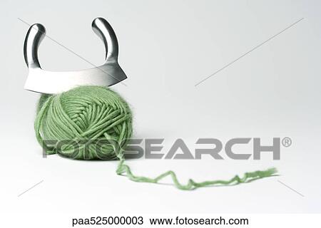 Stock Image - Mincing knife cutting into skein of green yarn. Fotosearch