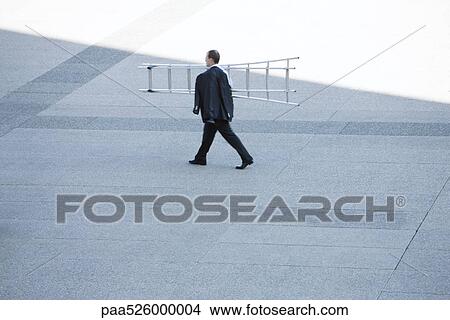 Picture - Businessman carrying ladder on shoulder across public square. Fotosearch