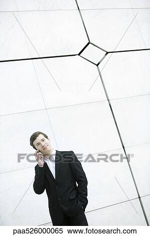 Businessman using cell phone, hand in pocket, casually standing by wall View Large Photo Image Stock Photography - Businessman using cell phone, hand in pocket, casually standing by wall. Fotosearch