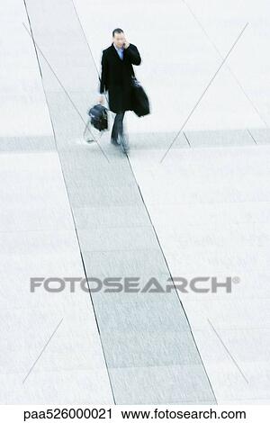 Stock Image - Businessman walking across public square talking on cell phone. Fotosearch