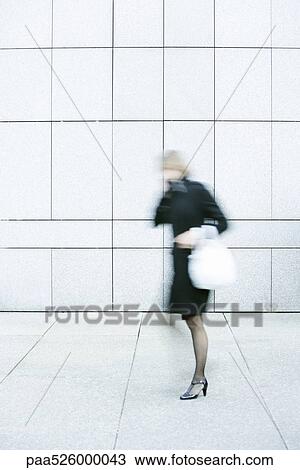 Stock Image - Businesswoman talking on phone while walking down sidewalk. Fotosearch