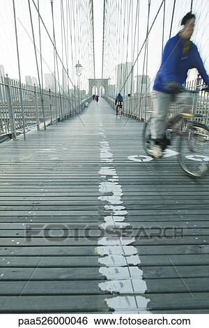 Man riding bike across pedestrian walkway of Brooklyn Bridge in New York City, Manhattan skyline in distance View Large Photo Image Stock Photograph - Man riding bike across pedestrian walkway of Brooklyn Bridge in New York City, Manhattan skyline in distance. Fotosearch