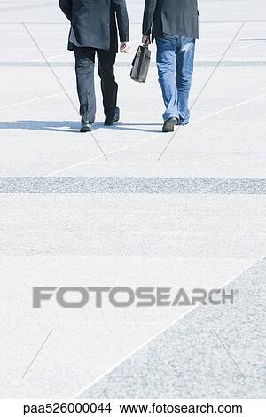 Two businessmen walking together wearing business attire, one wearing jeans with blazer View Large Photo Image Picture - Two businessmen walking together wearing business attire, one wearing jeans with blazer. Fotosearch