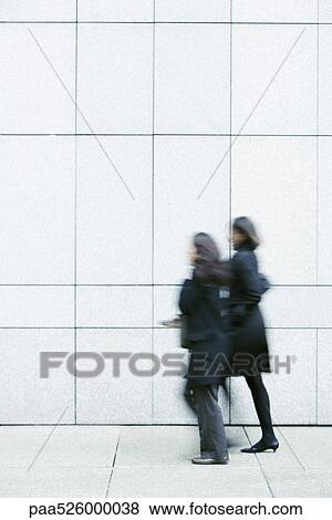 Two businesswomen walking side by side down sidewalk View Large Photo Image Stock Photo - Two businesswomen walking side by side down sidewalk. Fotosearch