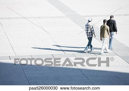 Young men walking together across public square View Large Photo Image Stock Image - Young men walking together across public square. Fotosearch