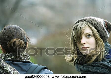 Young woman walking with friend in park, looking over shoulder at camera View Large Photo Image Stock Photo - Young woman walking with friend in park, looking over shoulder at camera. Fotosearch