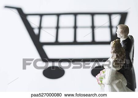 Stock Image - Bride and groom figures looking at shopping cart. Fotosearch