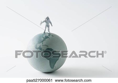 Stock Image - Miniature astronaut standing on top of globe. Fotosearch
