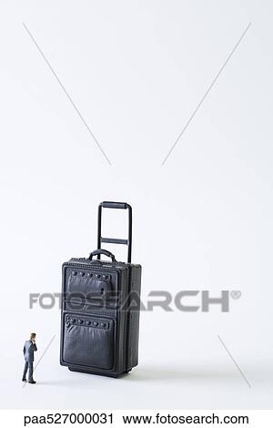 Stock Image - Miniature businessman facing large suitcase. Fotosearch