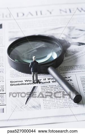 Picture - Miniature businessman standing before magnifying glass on newspaper. Fotosearch