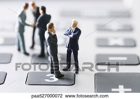 Stock Image - Miniature businessmen negotiating on calculator. Fotosearch