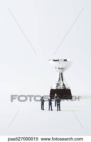 Stock Photography - Miniature businessmen standing face to face in front of trophy. Fotosearch