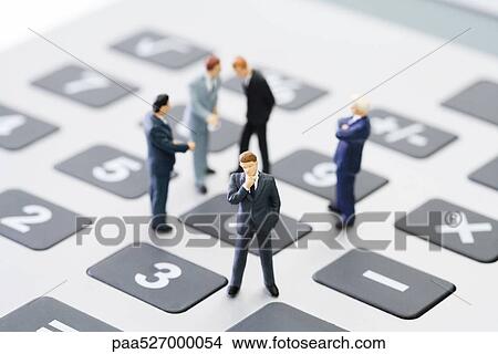 Picture - Miniature businessmen standing on calculator. Fotosearch