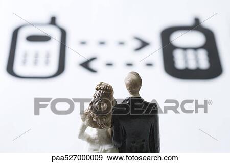 Stock Photo - Miniature couple looking at cell phone graphics with arrows between them. Fotosearch