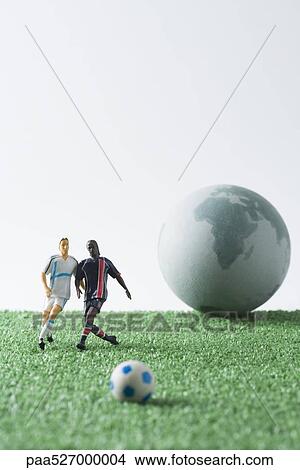 Picture - Miniature soccer players chasing soccer ball, globe in background. Fotosearch
